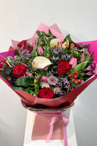 Forever in Love - Forever in Love, a vibrant hand-tied bouquet featuring classic red roses and soft pink tulips, complemented by delicate alstroemeria, textured statice, striking anthurium and clusters of red hypericum berries. Finished with lush seasonal foliage and wrapped in elegant pink tones, it’s a rich, eye-catching design perfect for anniversaries and Valentine's Day.